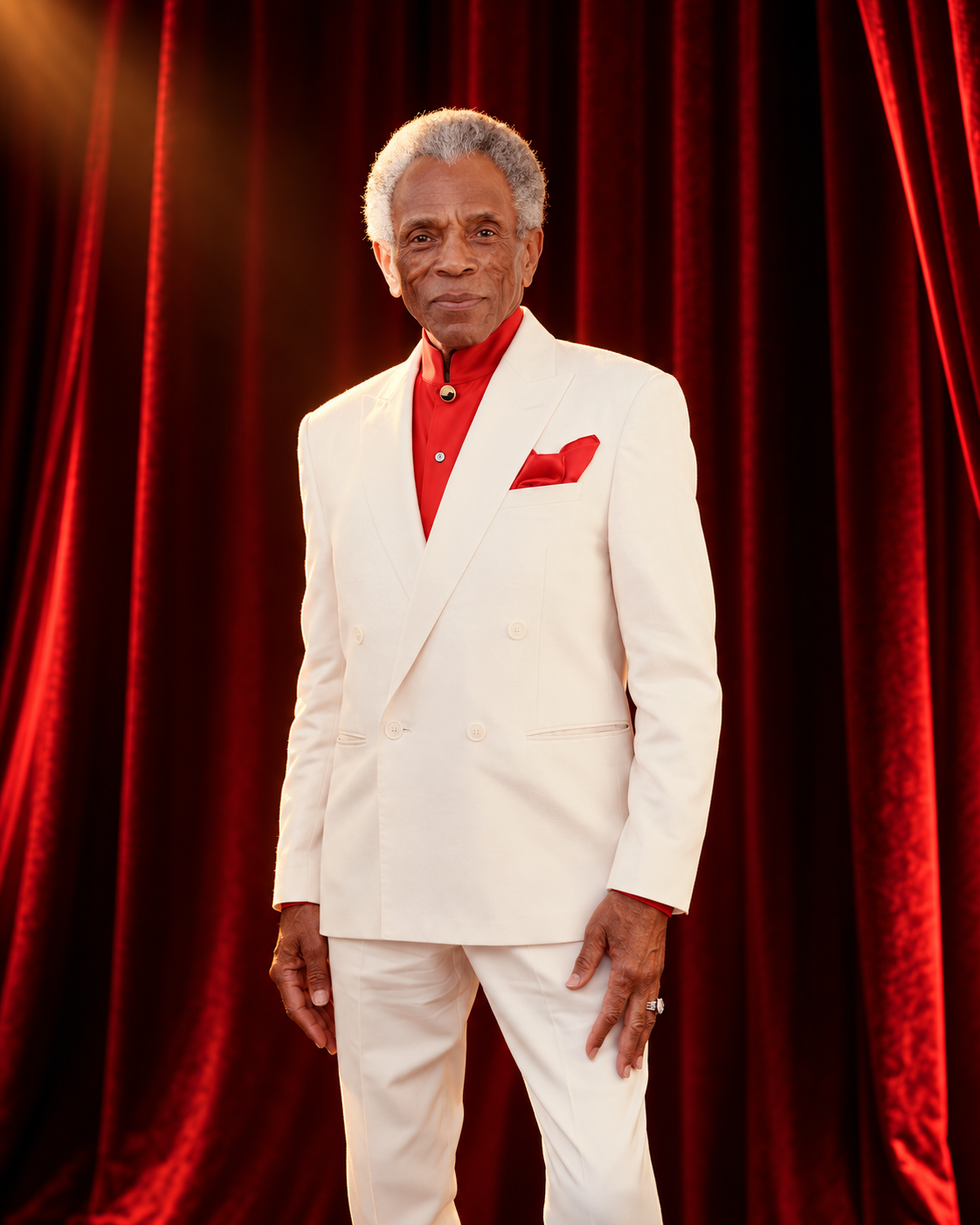 André De Shields in an ivory suit against a red velvet stage curtain.